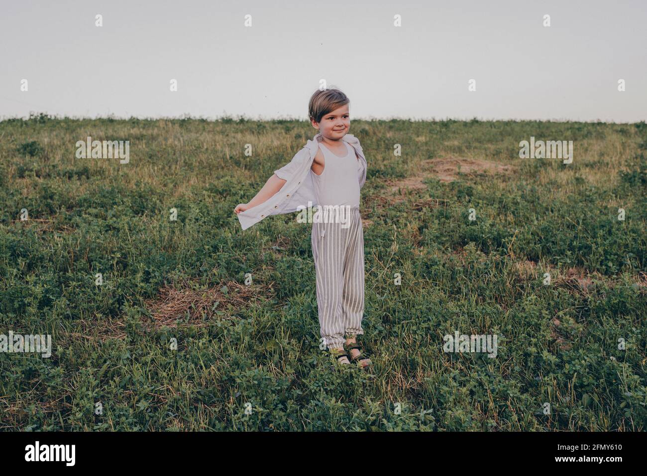 Portrait d'un heureux 5 ans petit mignon garçon, portant une chemise blanche debout dans le champ sur l'herbe verte Banque D'Images