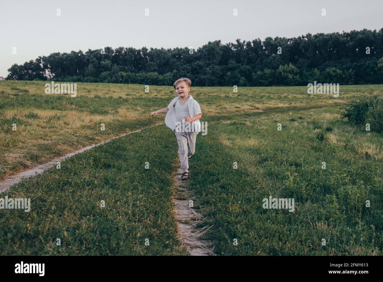 Portrait d'un heureux 5 ans petit mignon garçon, portant une chemise blanche courant dans le champ sur l'herbe verte Banque D'Images