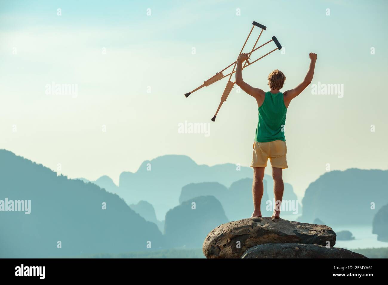 L'homme handicapé se tient sur le grand rocher dans la posture du gagnant et regarde la mer et les montagnes. Concept de soins de santé ou d'assurance Banque D'Images