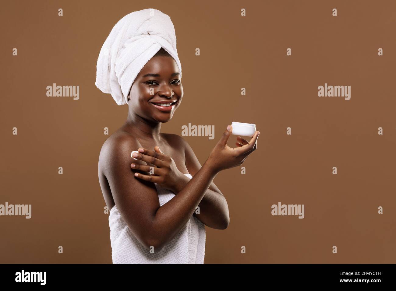 Concept d'autosoins. Belle dame noire avec serviette sur la tête appliquant une crème hydratante Banque D'Images