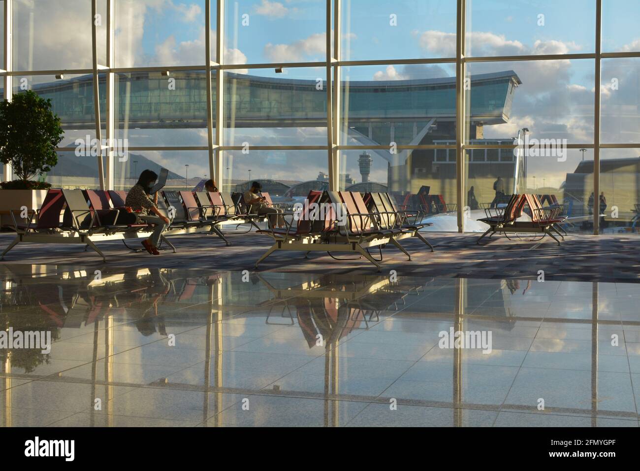 Quelques passagers attendent leur vol devant une immense fenêtre offrant une vue sur Chek Lap Kok, l'aéroport international de Hong Kong. Banque D'Images