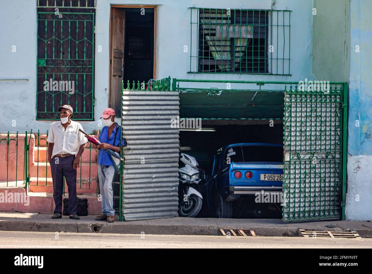 Deux hommes cubains portant un masque facial près d'une porte de garage ouverte à Santiago de Cuba, Cuba. C'est le moment de la pandémie de Covid-19 Banque D'Images