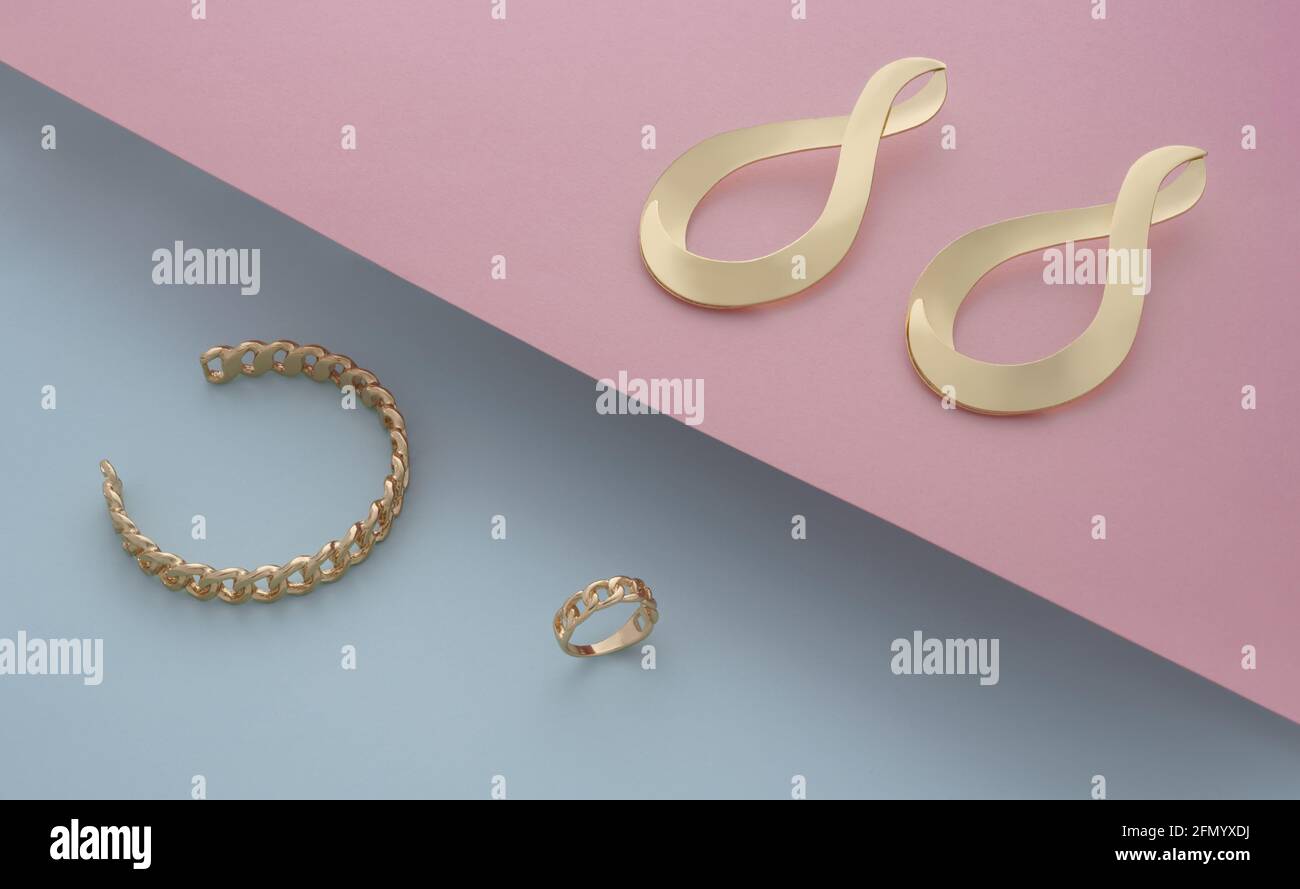 Bijoux d'or de boucles d'oreilles paire et bracelet sur rose et bleu Banque D'Images