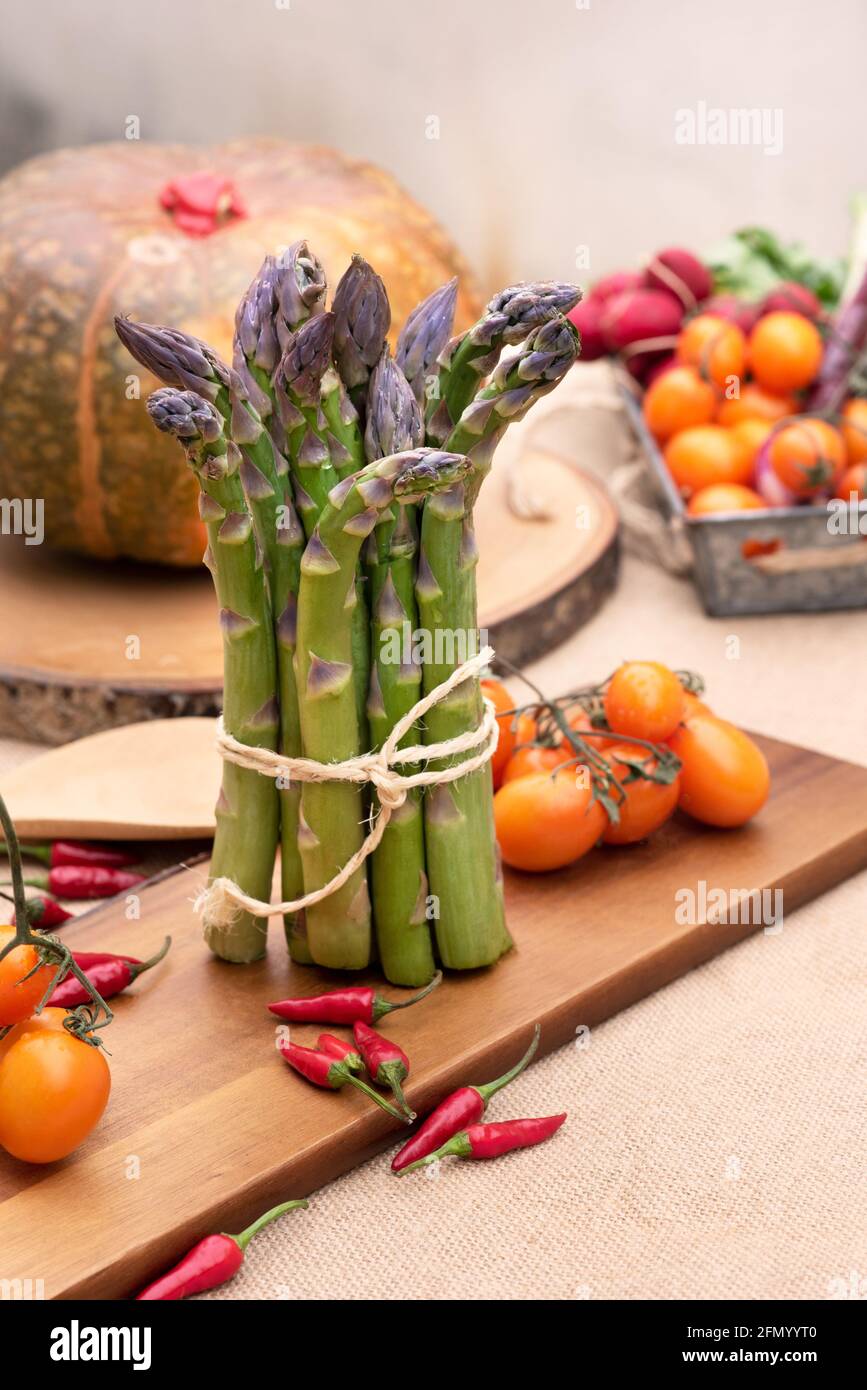 Asperges vertes fraîches isolées sur une vieille table en bois avec des tomates et une citrouille Banque D'Images