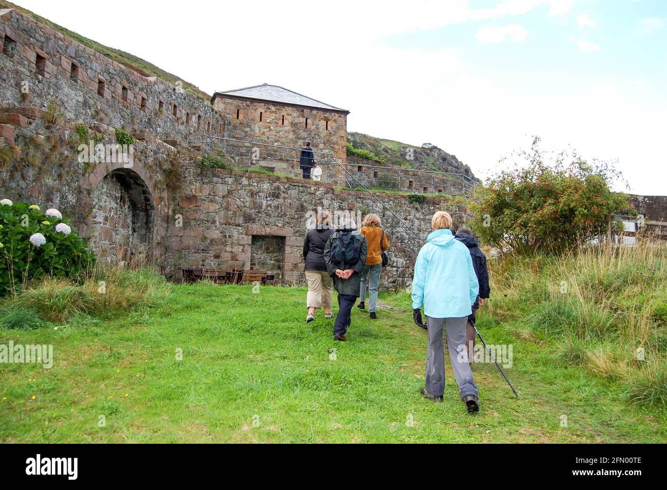 Promeneurs près de la forteresse des murs d'arche dans Jersey Channel Islands sentier de randonnée bâton château voûte remparts colline haut personnes personne météo buissons Bush Banque D'Images