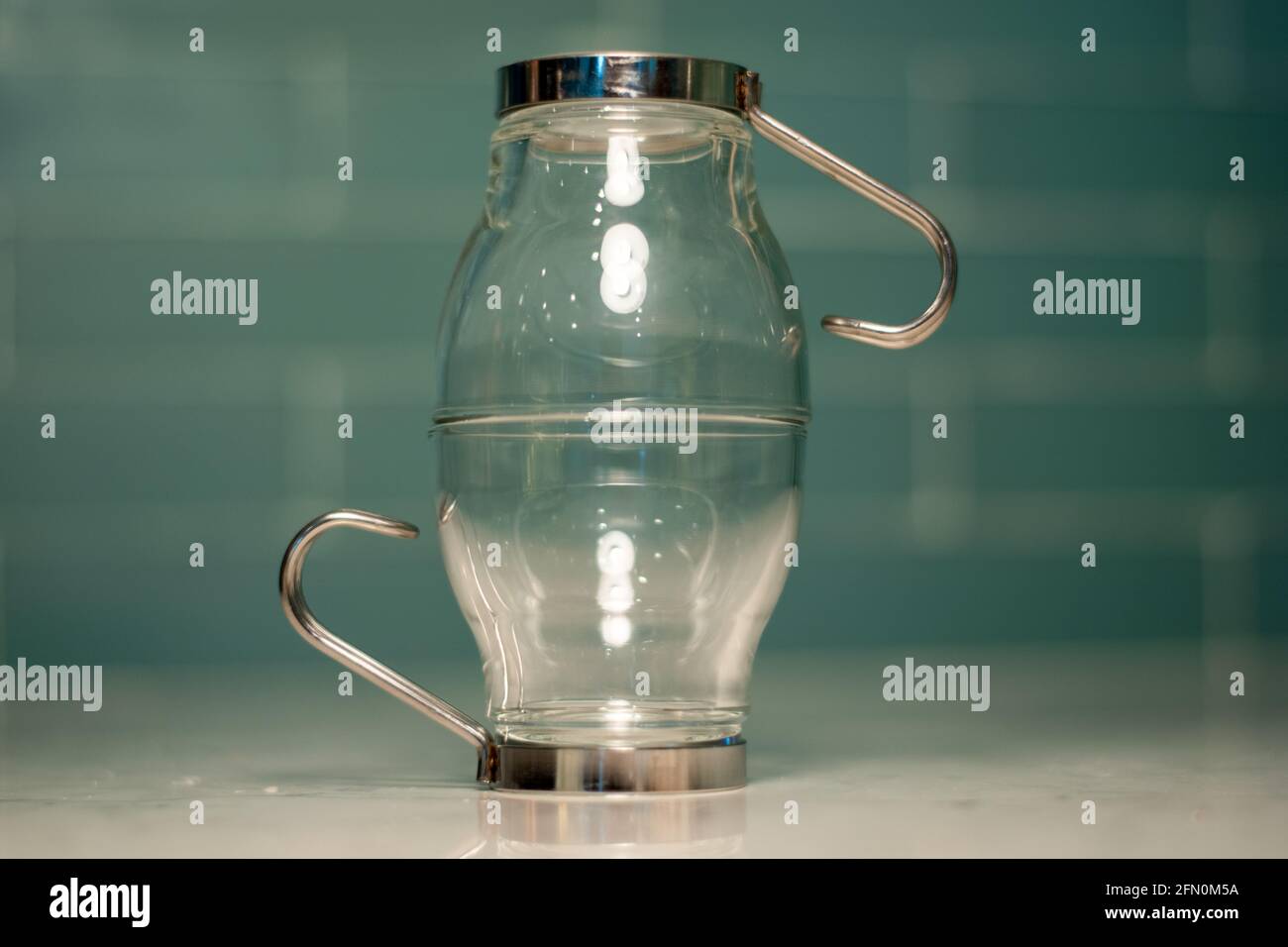 Photo abstraite de deux verres à espresso empilés/tournés vers l'extérieur. Verrerie et décoration intérieure avec fond de carrelage bleu et comptoir en granit. Banque D'Images