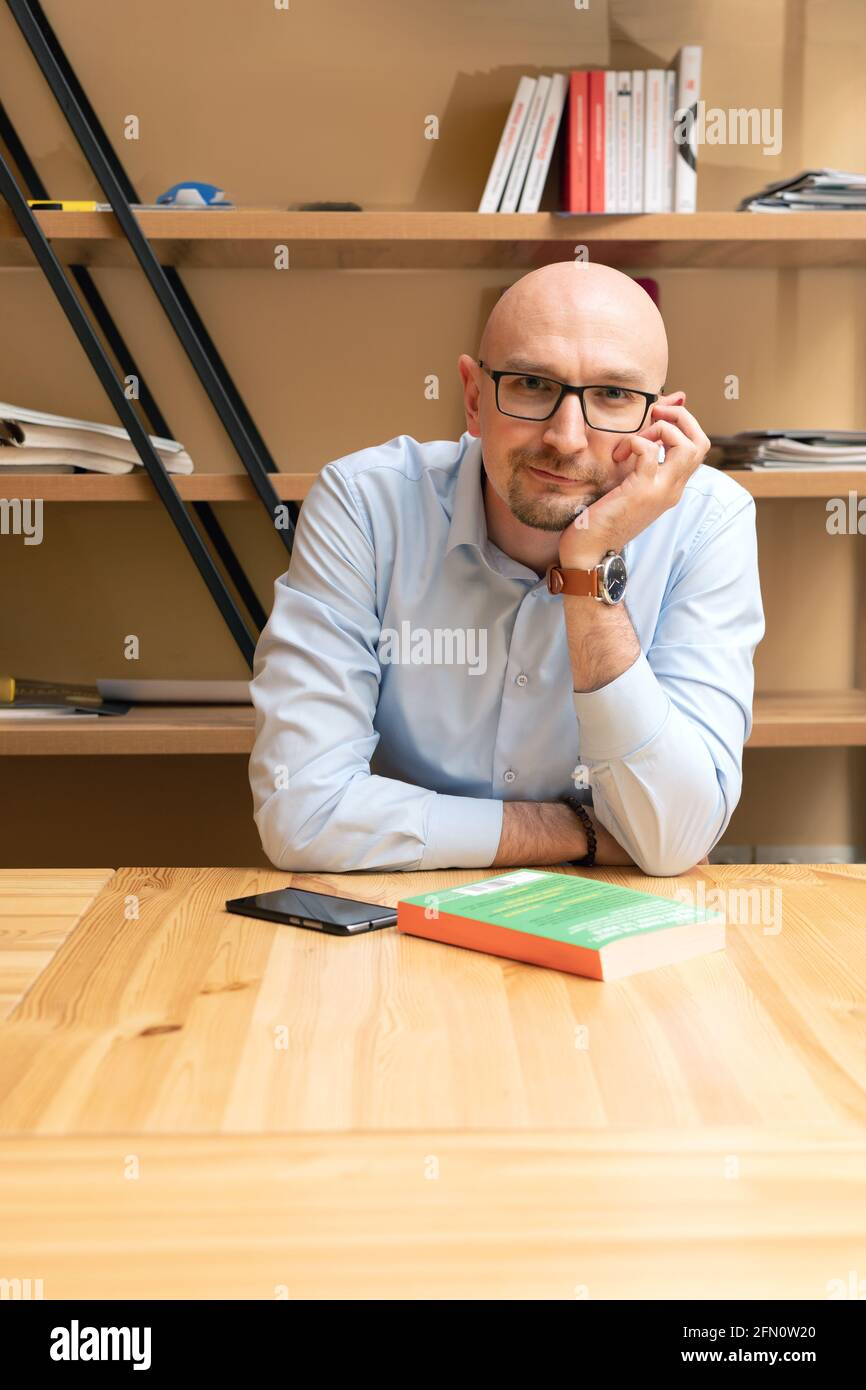 Souriant homme chauve sympathique portant des lunettes avec livre regardant appareil photo Banque D'Images