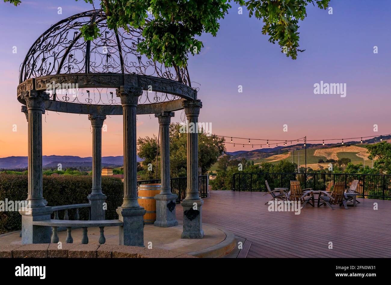 Des chaises en plein air et une table sur une terrasse en bois au coucher du soleil au printemps avec des vignes et des collines en arrière-plan, Napa Valley, Californie Etats-Unis Banque D'Images