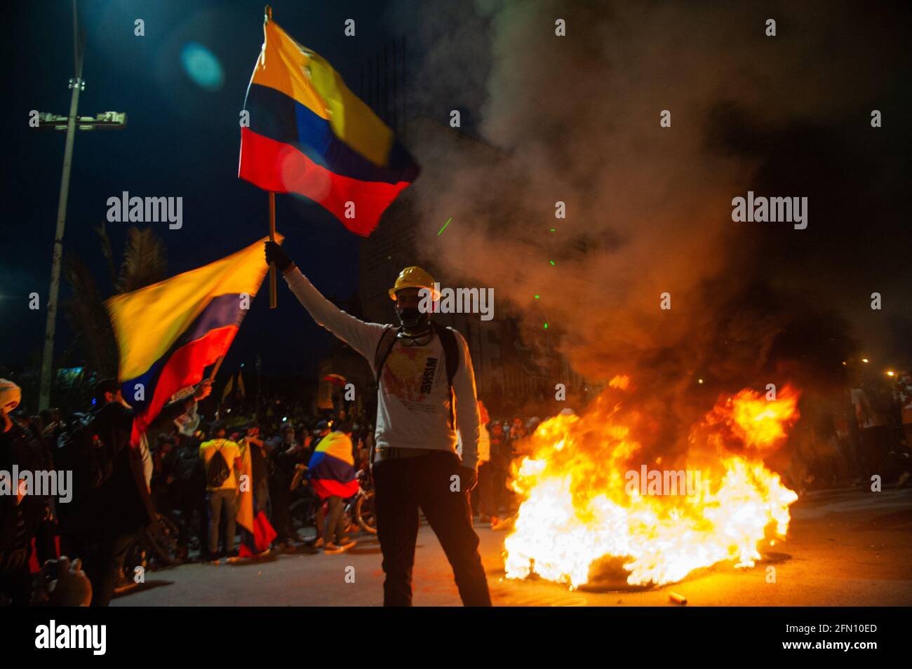 Bogota, Cundinamarca, Colombie. 12 mai 2021. Un démonstrateur fait passer un drapeau colombien devant un feu de pneus à Bogota, en Colombie, qui entre dans sa troisième semaine de manifestations antigouvernementales contre le président Ivan Duque Marquez et les morts qui se résument à 40 dans des cas de brutalité policière lors de la grève nationale, le 12 mai 2021. Credit: CHEPA Beltran/LongVisual/ZUMA Wire/Alamy Live News Banque D'Images