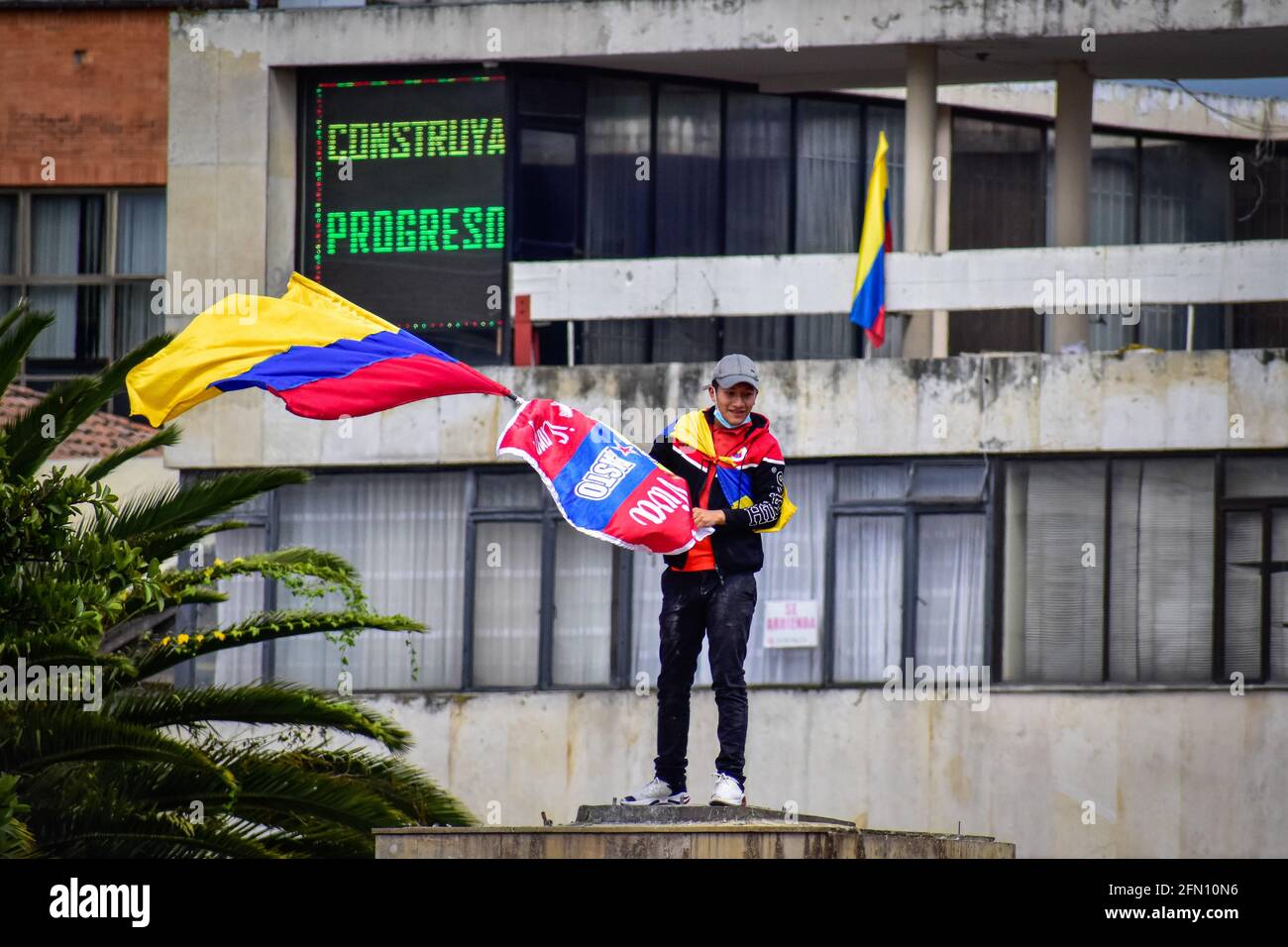 Pasto, Narino, Colombie. 12 mai 2021. Le Demostrator fait monter le drapeau de la Colombie à l'endroit où se trouvait la statue d'Antonio Narino, qui a été enlevée la nuit précédente avec une clôture derrière lui qui dit: ''construire le progrès'' dans le centre de la ville de Pasto, Narino le 12 mai 2021 crédit: Camilo Erasso/LongVisual/ZUMA Wire/Alamy Live News Banque D'Images