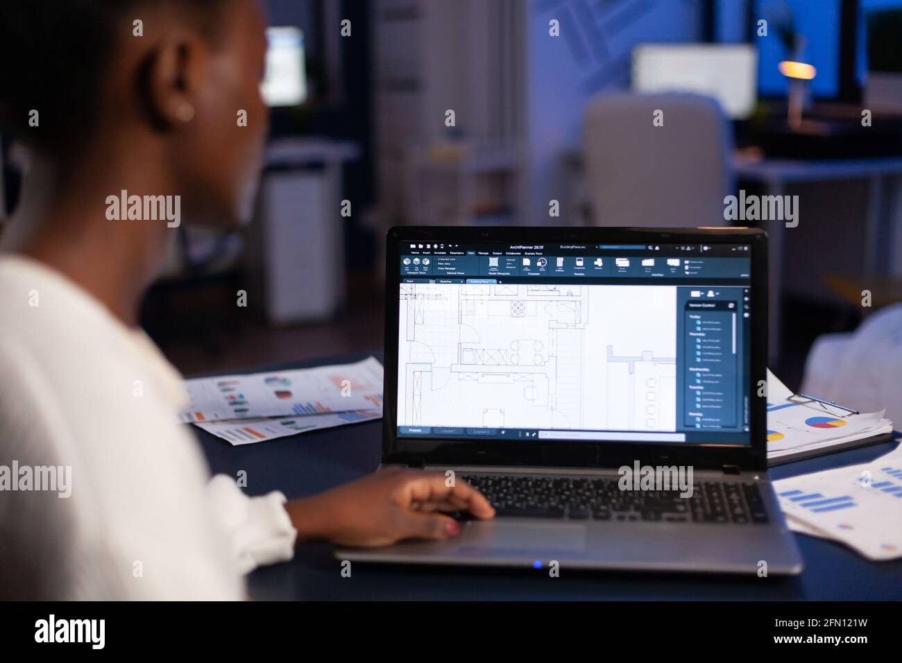 Vue sur l'épaule d'un architecte africain travaillant tard dans la nuit au bureau à l'aide d'un logiciel de CAO, imprimer en bleu. Employée d'une femme industrielle étudiant l'idée de prototype montrant le logiciel de CAO sur l'écran de l'appareil. Banque D'Images