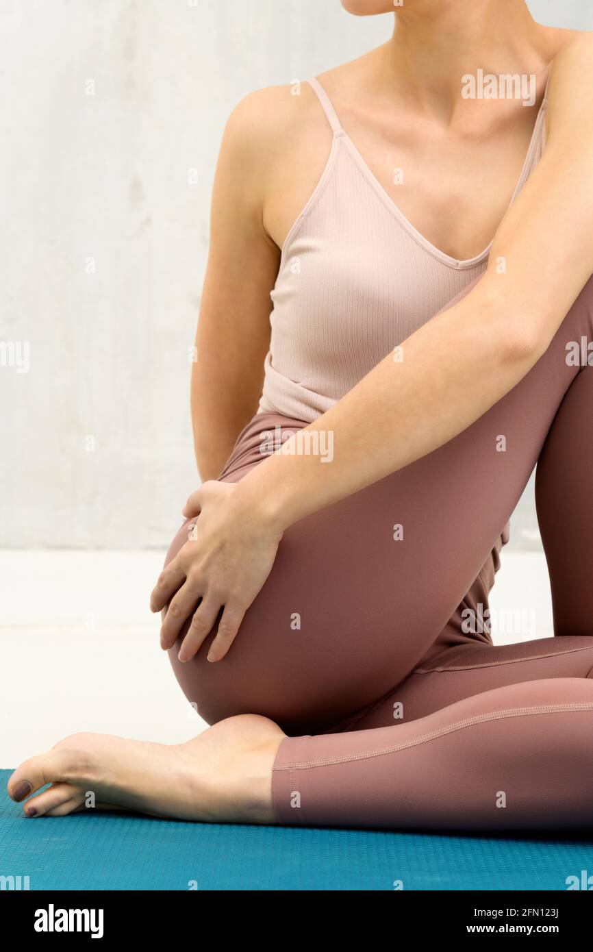 Gros plan rogné d'une femme anonyme dans un Marichyasana variation yoga pose la torsion pour saisir sa cuisse dedans un concept de santé et de forme physique Banque D'Images