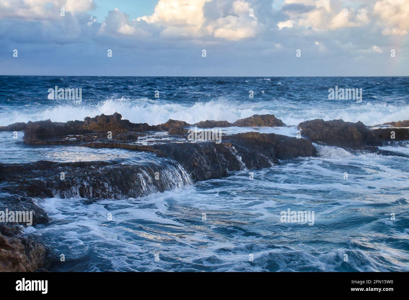 L'eau sur des rochers dans l'océan bleu au coucher du soleil à Qawra, Malte. Banque D'Images