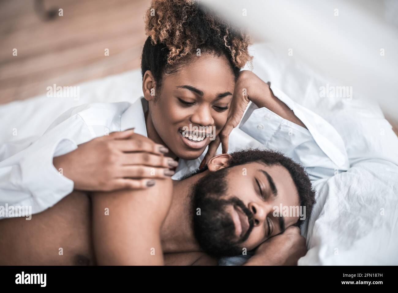 Femme heureuse touchant l'homme endormi dans le lit Banque D'Images