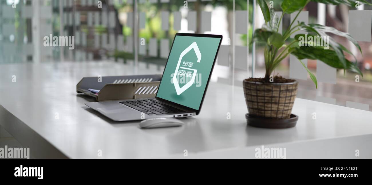 Vue latérale du bureau avec ordinateur portable maquette, bacs de rangement en papier et pot de plantes décorés dans une salle de bureau Banque D'Images