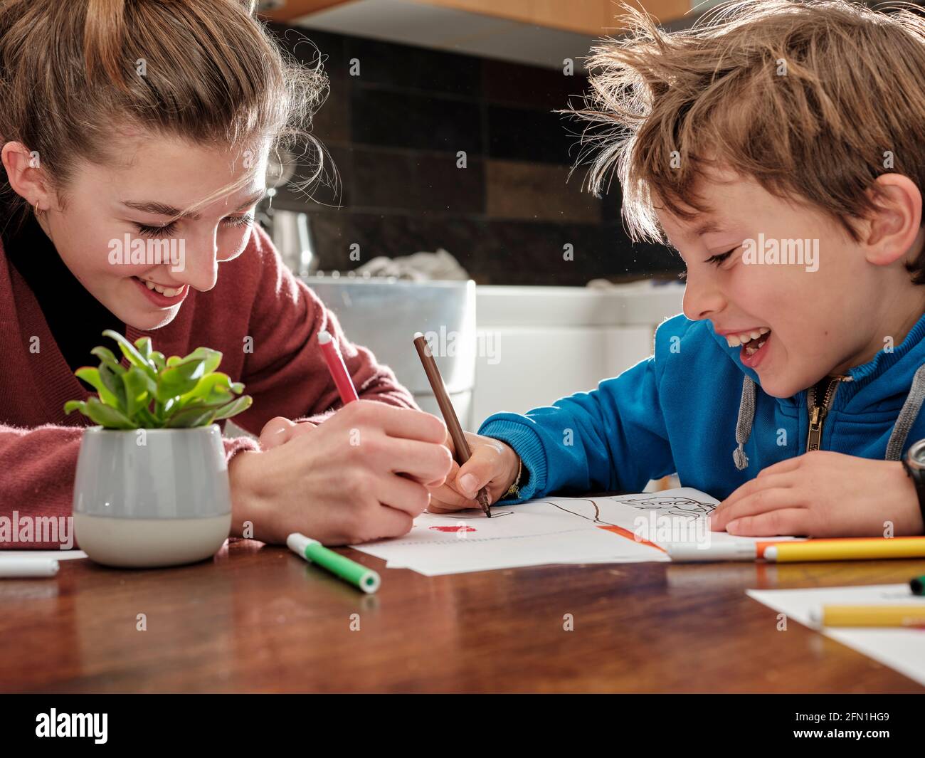Les enfants tirent sur des feuilles de papier avec des crayons et des marqueurs, assis à la table dans la cuisine à la maison. Banque D'Images