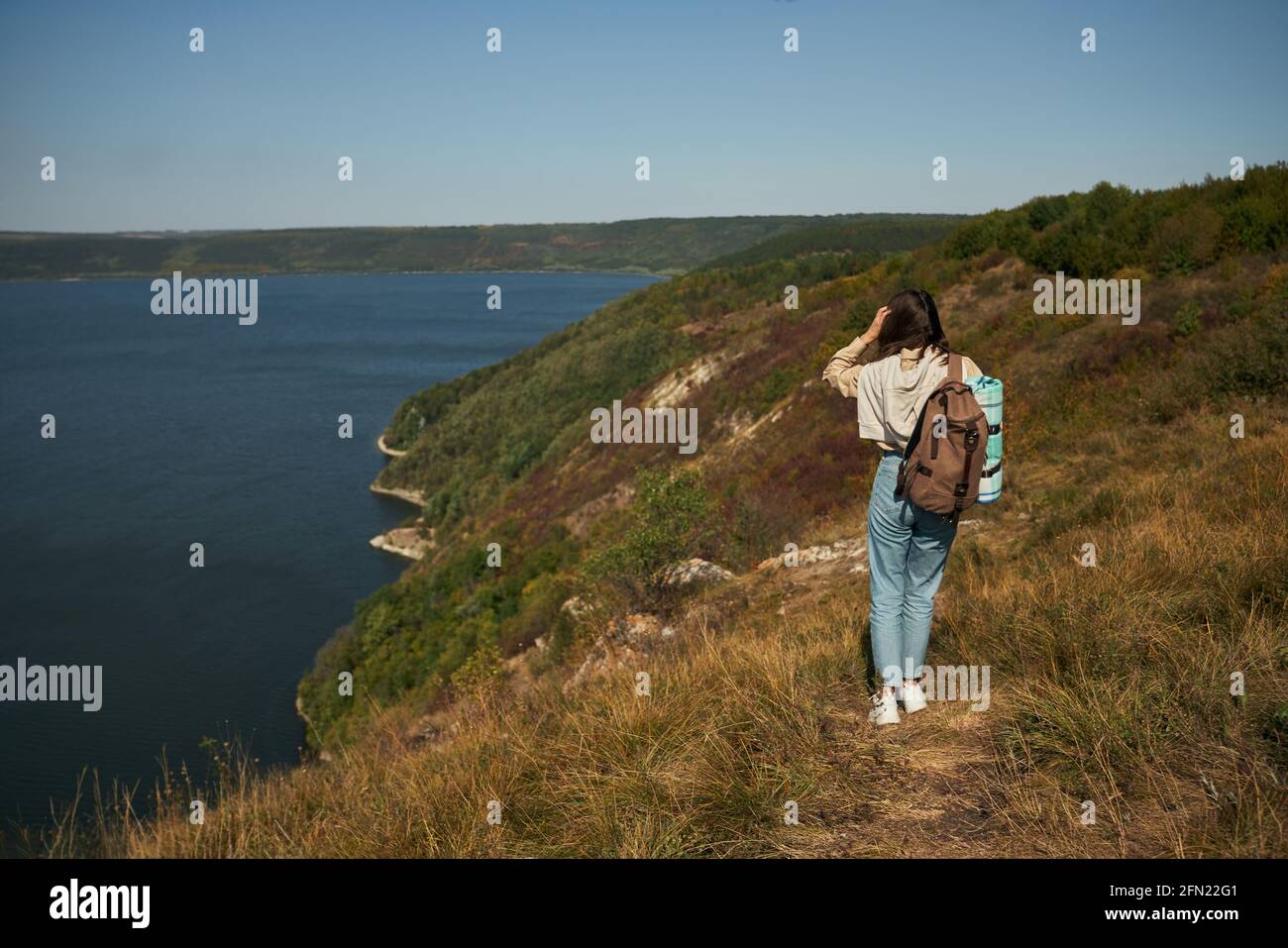 Vue arrière de la jeune femme avec sac à dos marchant le long de la haute colline verte au canyon de Dniester. Une femme voyage à la découverte de beaux endroits en Ukraine lors de la randonnée seule. Banque D'Images