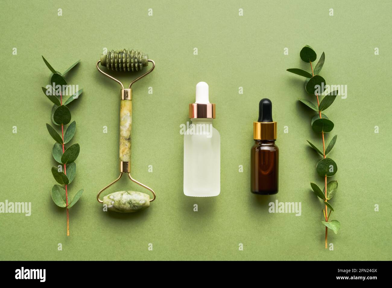 Rouleau de massage vert de jade facial, flacons compte-gouttes en verre à usage médical et cosmétique, et eucalyptus sur fond vert. Concept SPA. Vue de dessus, cop Banque D'Images