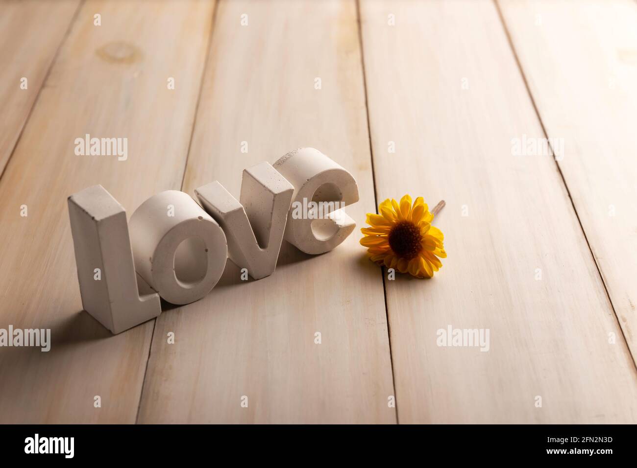 Image conceptuelle de lettres concrètes disant Amour avec un jaune fleur sur panneau blanc en bois lavé avec espace de copie Banque D'Images