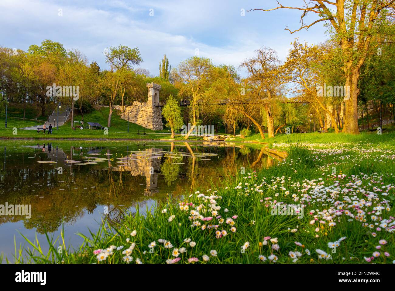 Photo prise dans le parc Nicolae Romanescu de Craiova, Roumanie au coucher du soleil. La photo se compose d'un étang, d'un pré avec des fleurs et d'un pont suspendu Banque D'Images