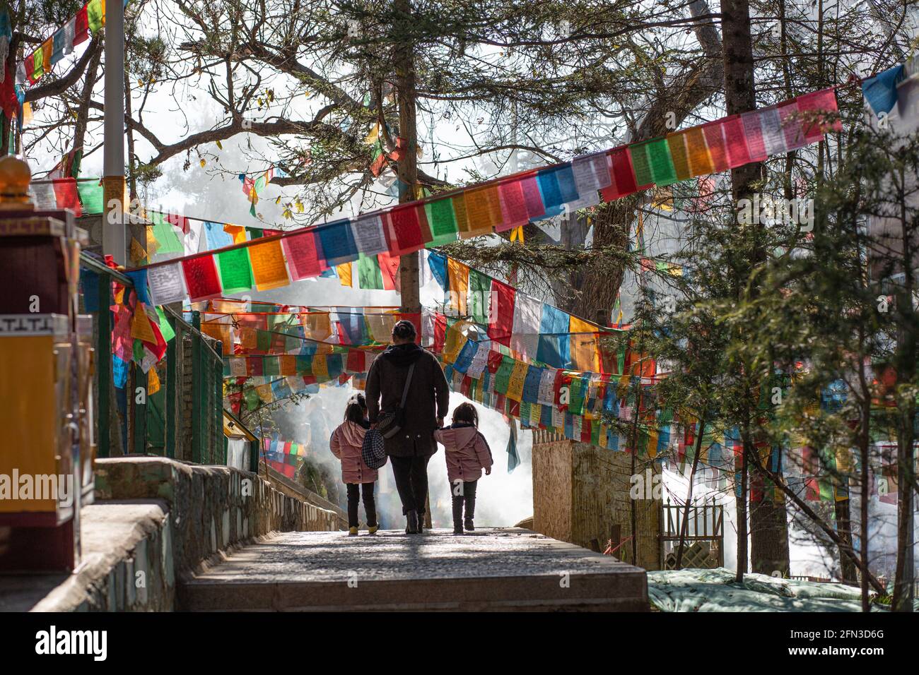 Femme vue de derrière marchant avec ses deux enfants au milieu des drapeaux de prière.Shangri la, Yunan. République populaire de Chine 2019 Banque D'Images