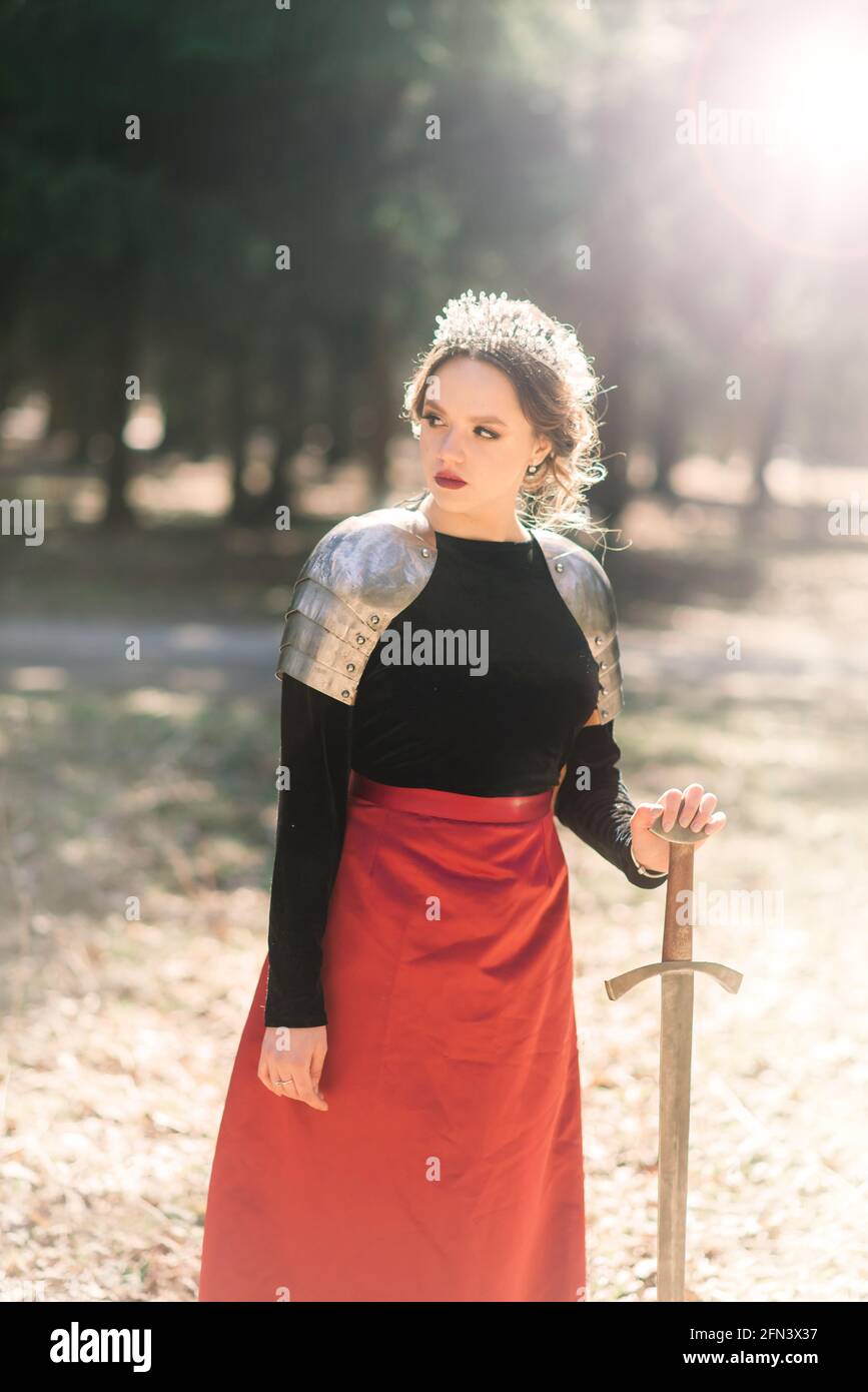Femme médiévale armée guerrier en armure posant sur fond de forêt et de coucher de soleil. Banque D'Images