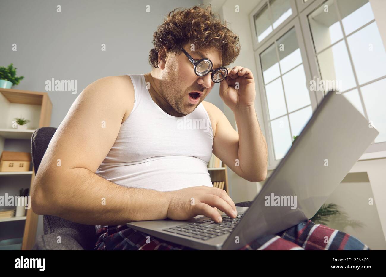 Surprise drôle choqué gros homme en pyjama lit des nouvelles étonnantes sur ordinateur portable Banque D'Images