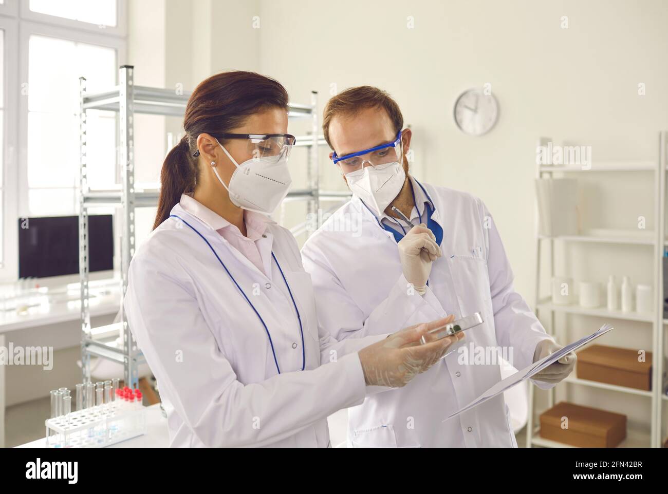 Deux scientifiques dans les masques protecteurs prennent des notes comme ils examinent cultures de bactéries dans la boîte de petri Banque D'Images