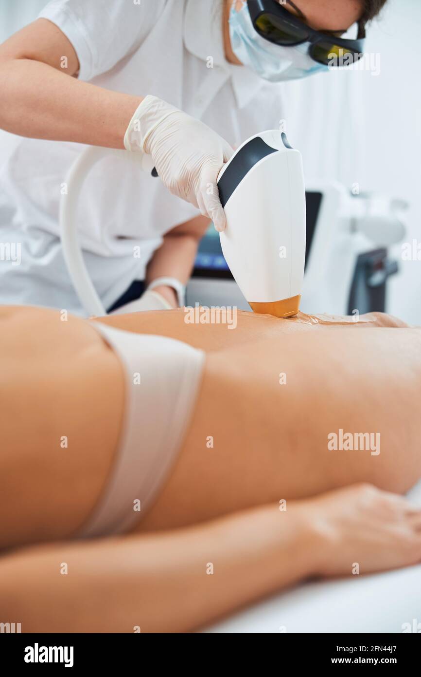 Dermatologue professionnel effectuant l'épilation au laser sur les jambes du patient Banque D'Images
