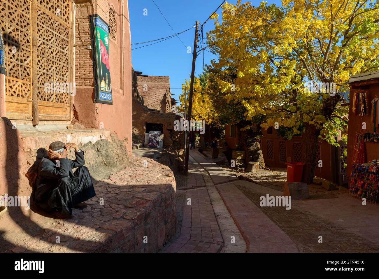 Homme résident assis contre un mur et profitant du soleil d'automne dans l'ancien village Abyaneh, province d'Ispahan, Iran Banque D'Images