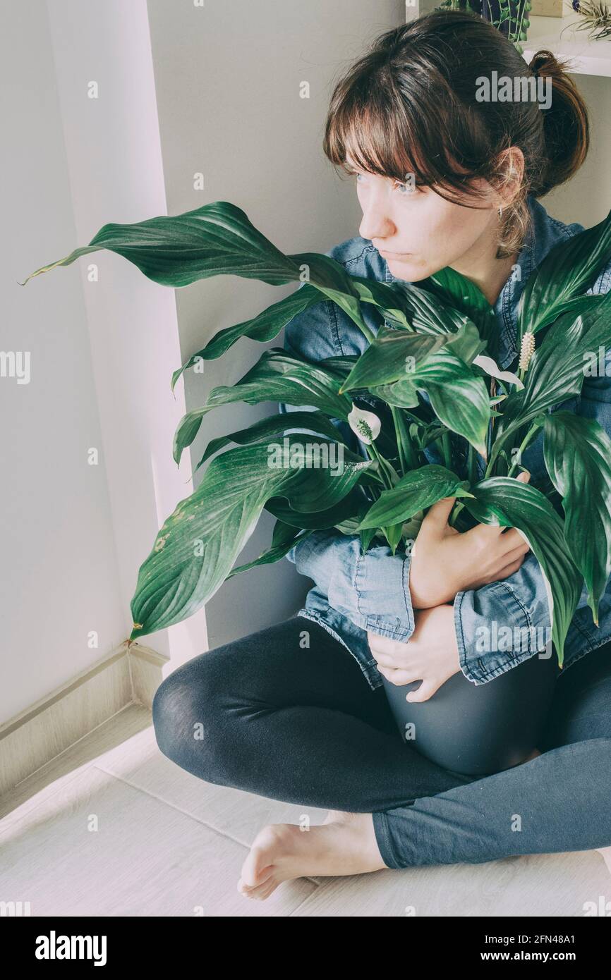 le portrait d'une femme aux cheveux bruns est assis sur le plancher de sa maison et embrasse une plante d'un pot Banque D'Images