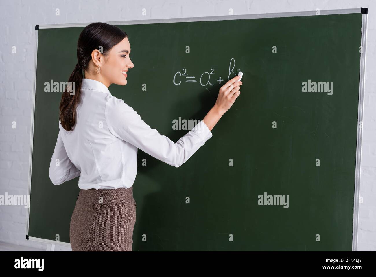 Professeur souriant écrivant l'équation mathématique sur tableau noir Banque D'Images