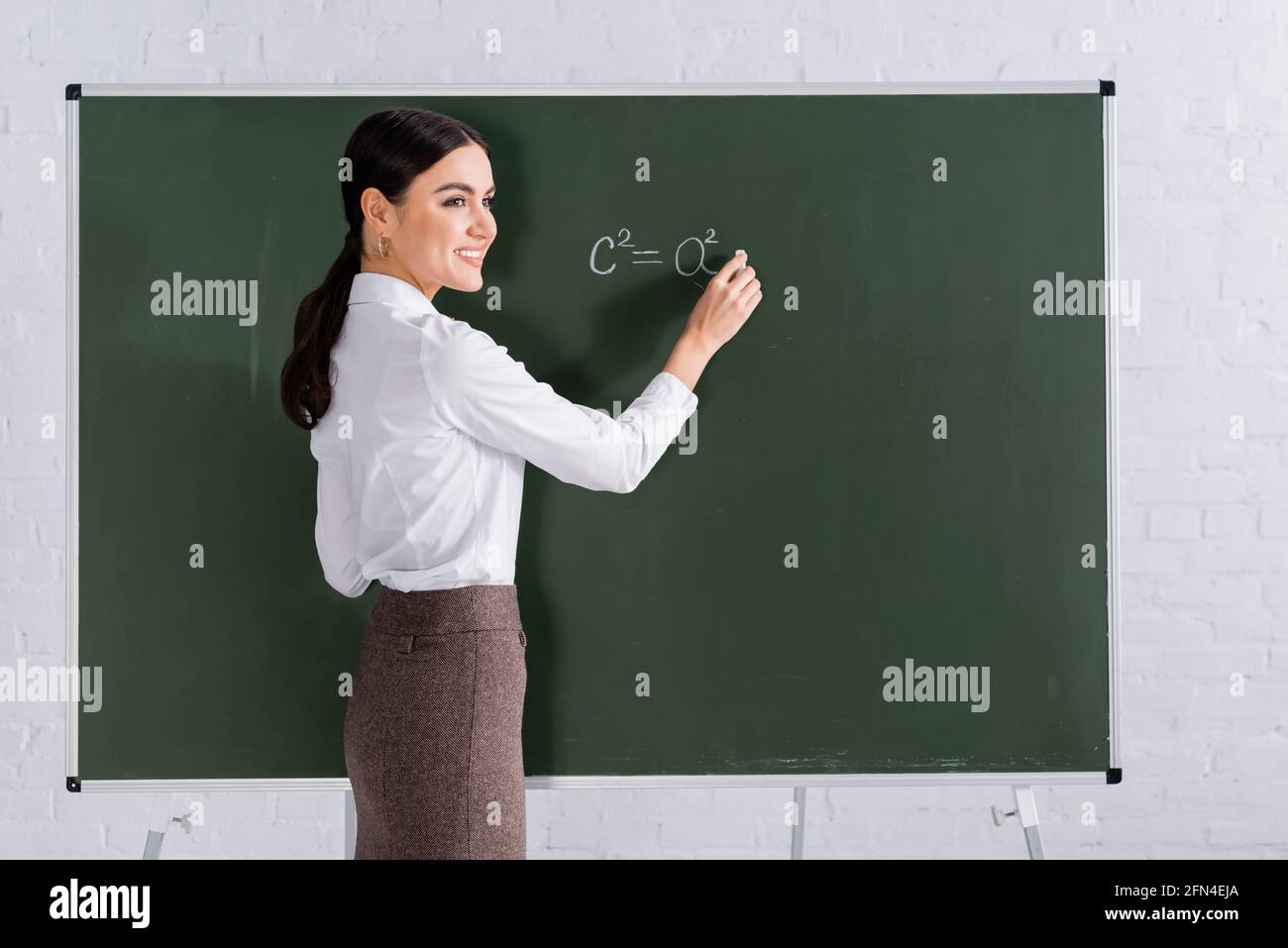 Professeur gai avec craie écrivant l'équation mathématique sur tableau noir Banque D'Images