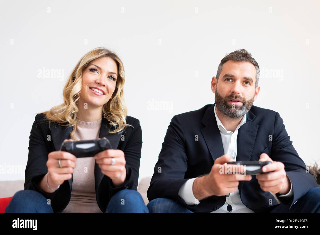 Couple élégant jouant à des jeux vidéo. Les gens d'affaires souriants s'amusent à la console pendant une pause. Développeurs de logiciels qui tiennent des joysticks. Banque D'Images
