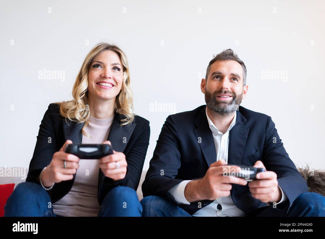 Couple élégant jouant à des jeux vidéo. Les gens d'affaires souriants s'amusent à la console pendant une pause. Développeurs de logiciels qui tiennent des joysticks. Banque D'Images