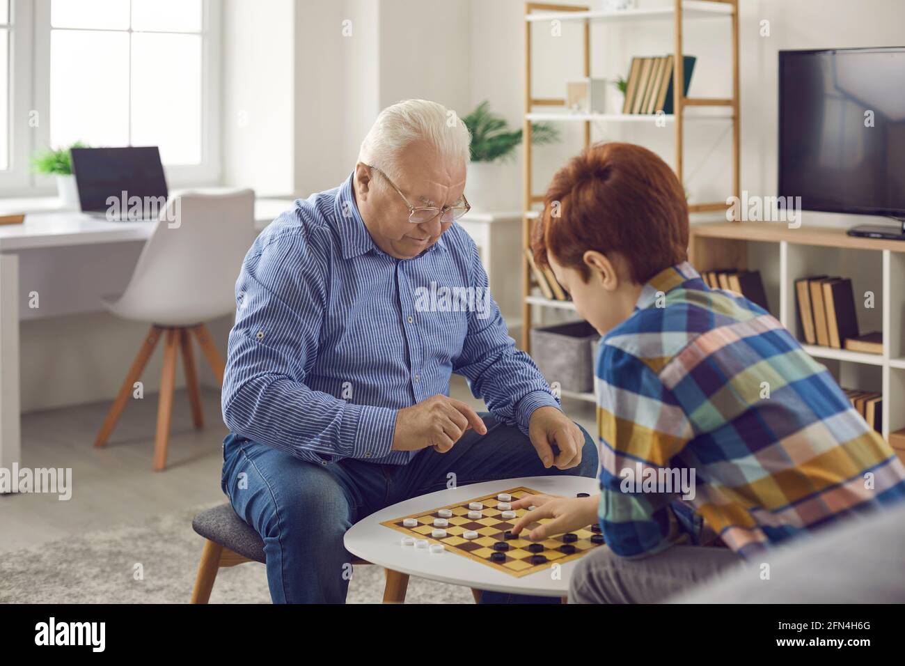 Senior homme concentrique grand-père assis et jouant des dames avec son petit-fils Banque D'Images