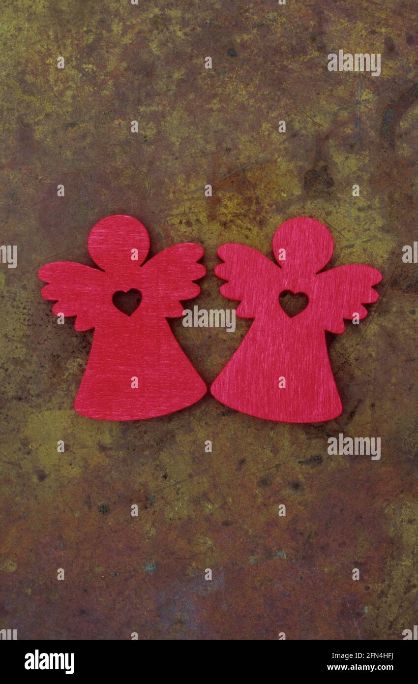 Deux découpes en bois de couleur rouge des anges avec des ailes et des coeurs à leurs centres, couchés sur du laiton terni Banque D'Images