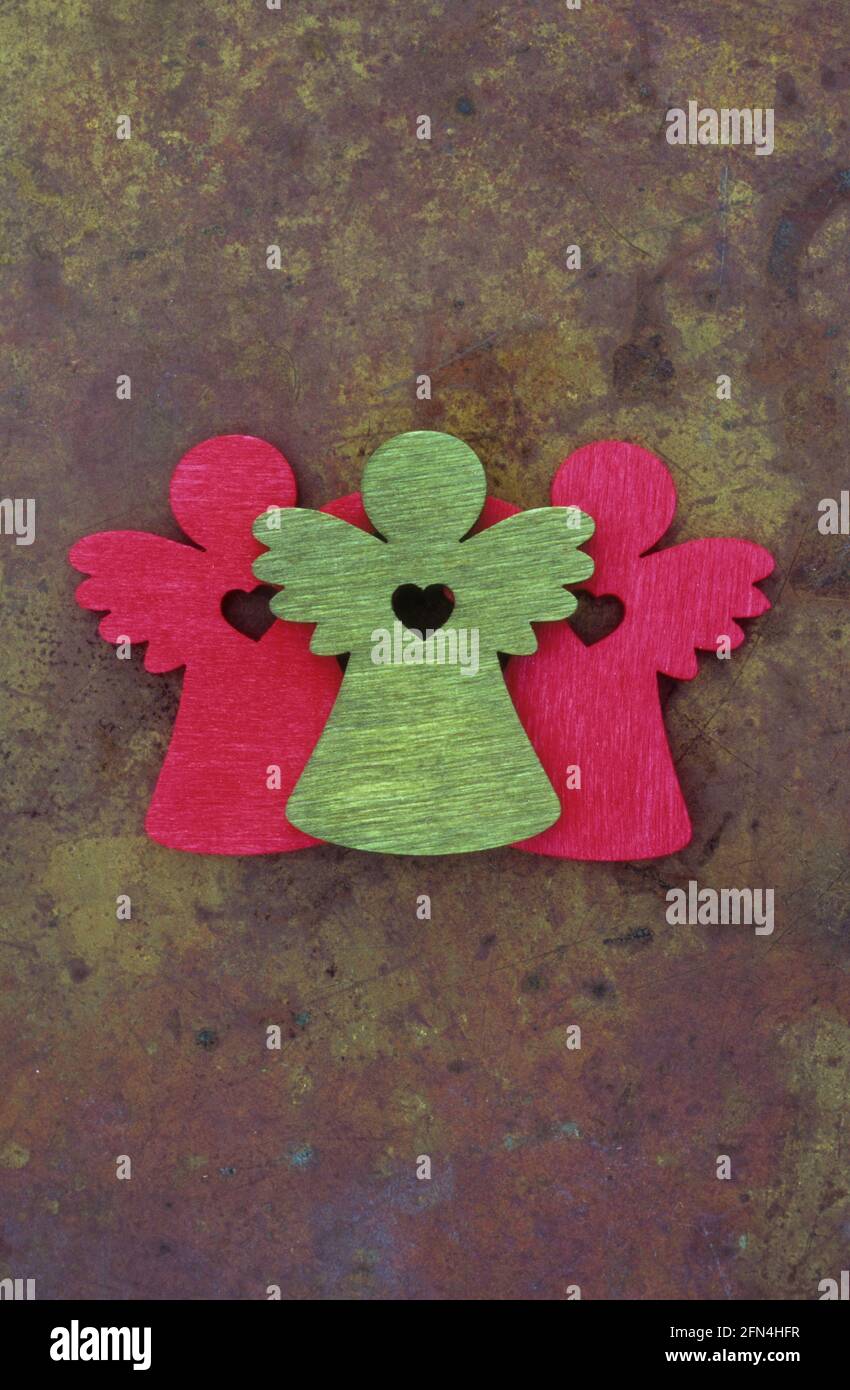 Deux découpes en bois de couleur rouge et un vert d'anges avec des ailes et des coeurs à leurs centres couchés sur du laiton terni Banque D'Images