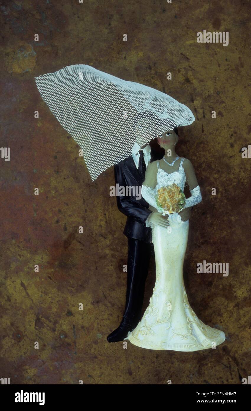 Modèle en plastique de mariée de mariage à la peau sombre et de marié debout à proximité avec voile étant soufflé sur leurs visages Banque D'Images