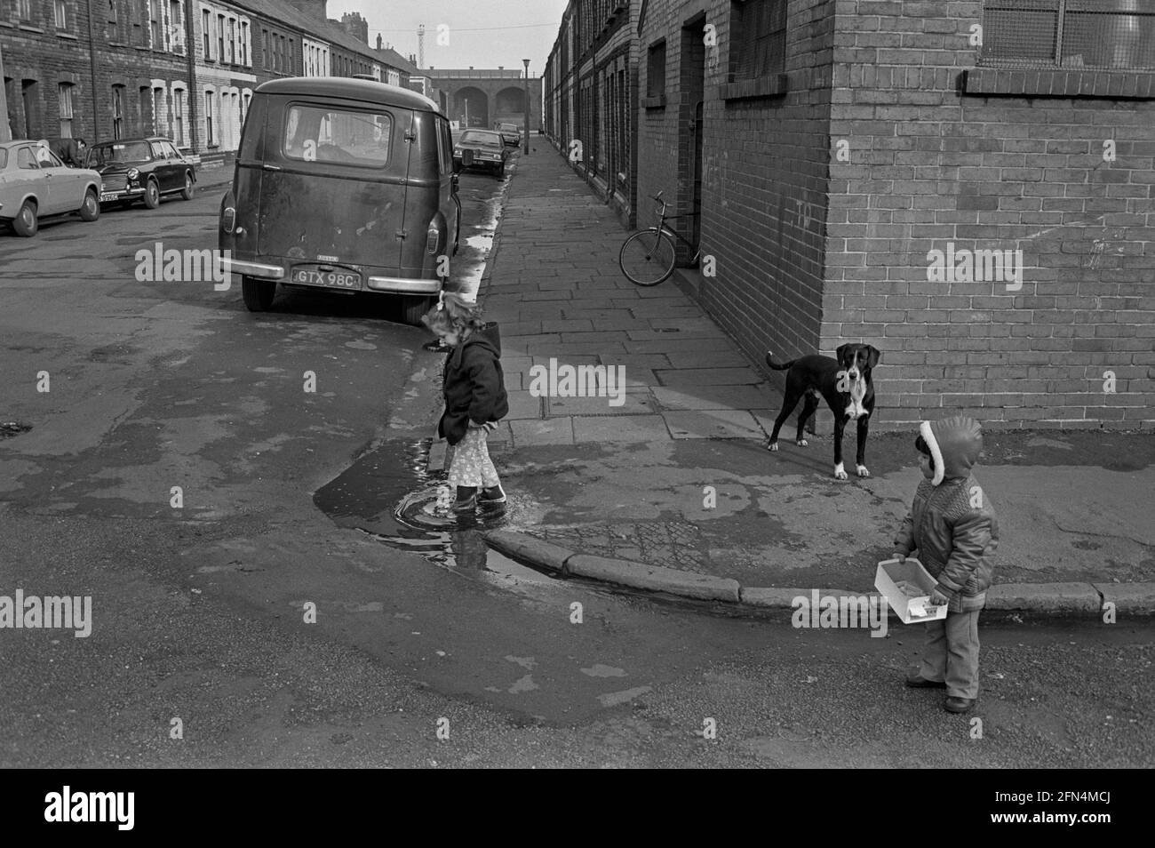 Un enfant pagayant dans une flaque au coin de la rue à Splott, Cardiff, 1974 Banque D'Images