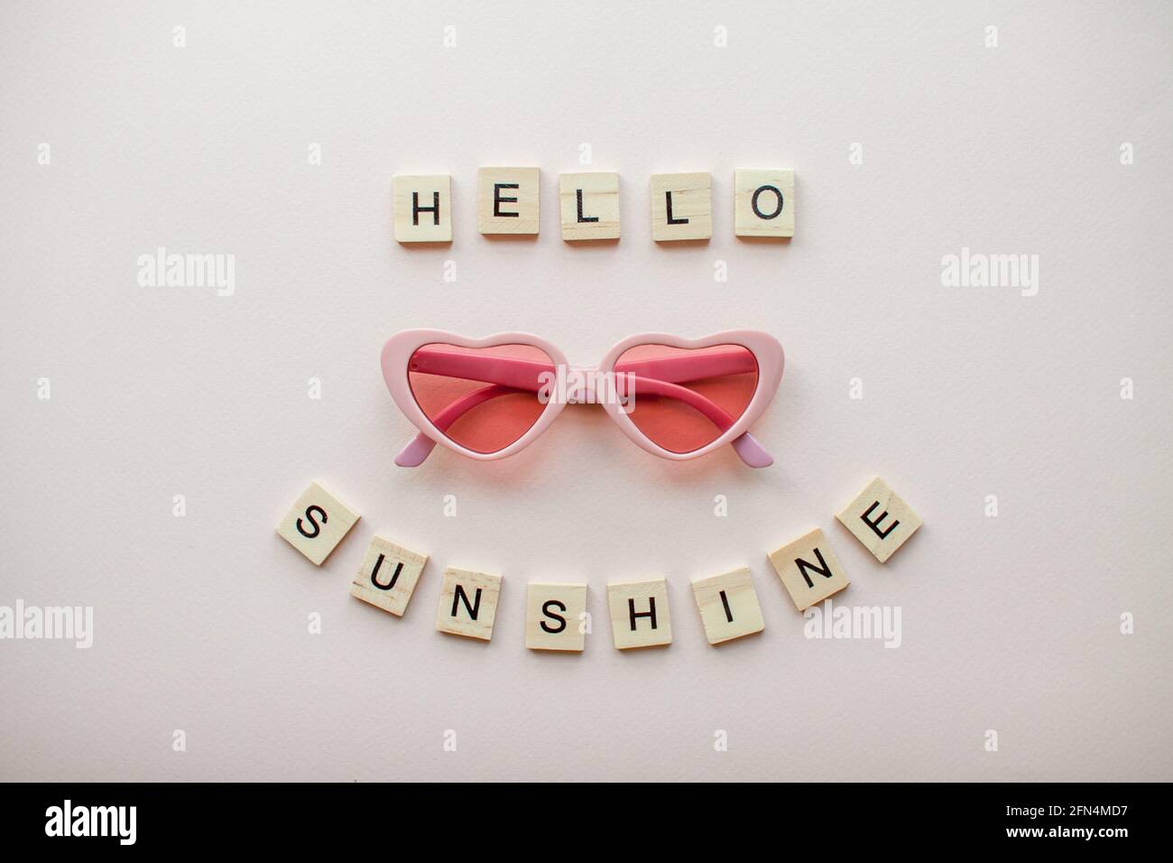 Mise en page. Verres roses sous forme de coeurs sur fond rose clair. Inscription de blocs de bois Hello Sunshine Banque D'Images