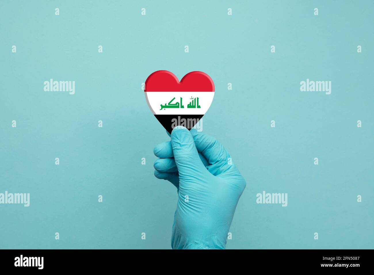 Mains portant des gants chirurgicaux de protection tenant le cœur du drapeau irakien Banque D'Images