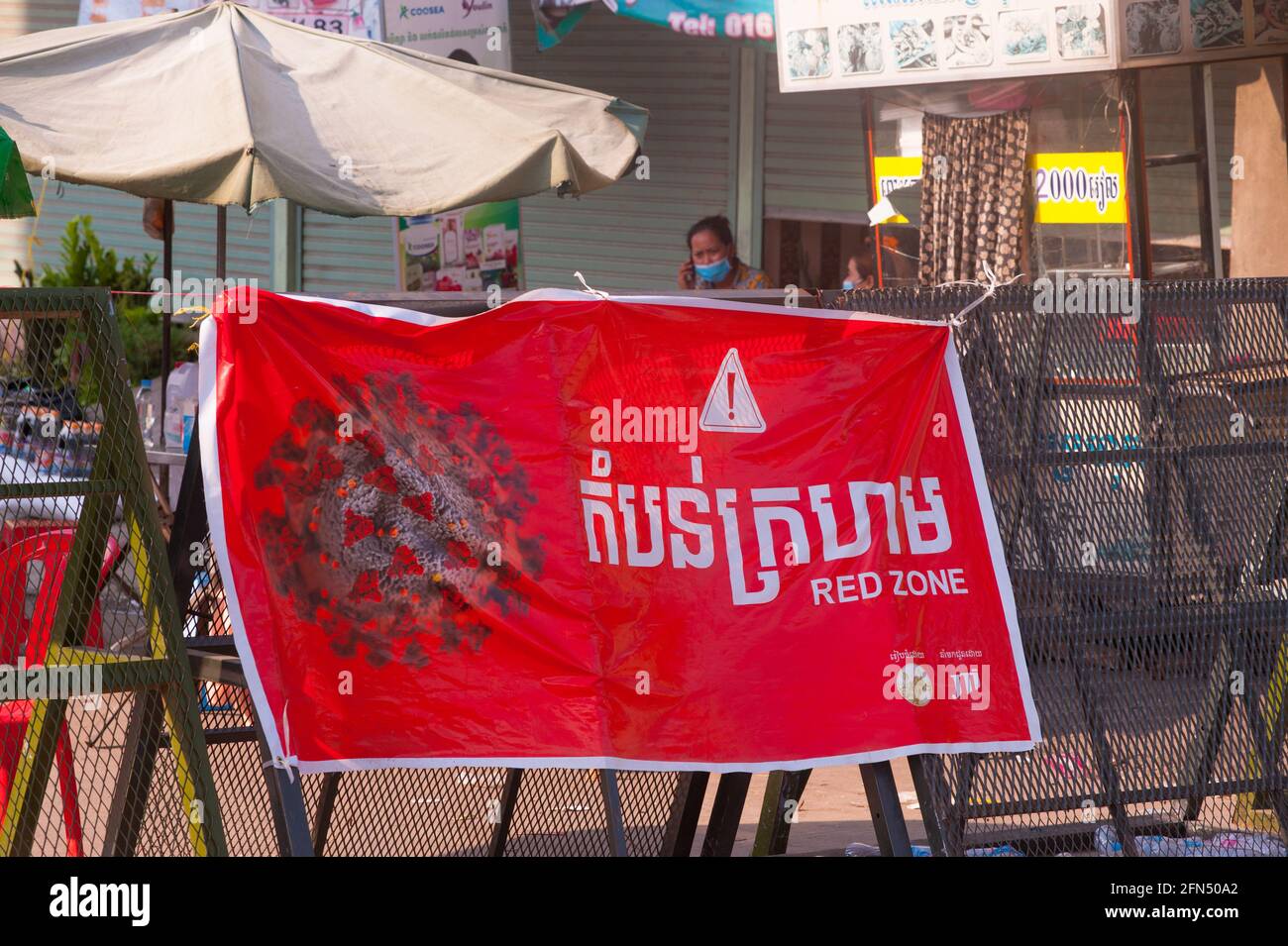 Phnom Penh, Cambodge. Le 14 mai 2021. Après 4 semaines de confinement total de la ville, le gouvernement continue de diviser Phnom Penh en 3 zones de couleur (rouge, orange et jaune) en raison de la poussée continue de COVID - 19. Une femme cambodgienne, portant un masque de protection, Parle sur son smartphone derrière un poste de contrôle de la police dans une « Red zone », ce qui signifie un risque élevé d'infection. Les Cambodgiens des zones rouges sont en quarantaine dans leurs rues. Credit: Kraig Lieb / Alamy Live News Banque D'Images