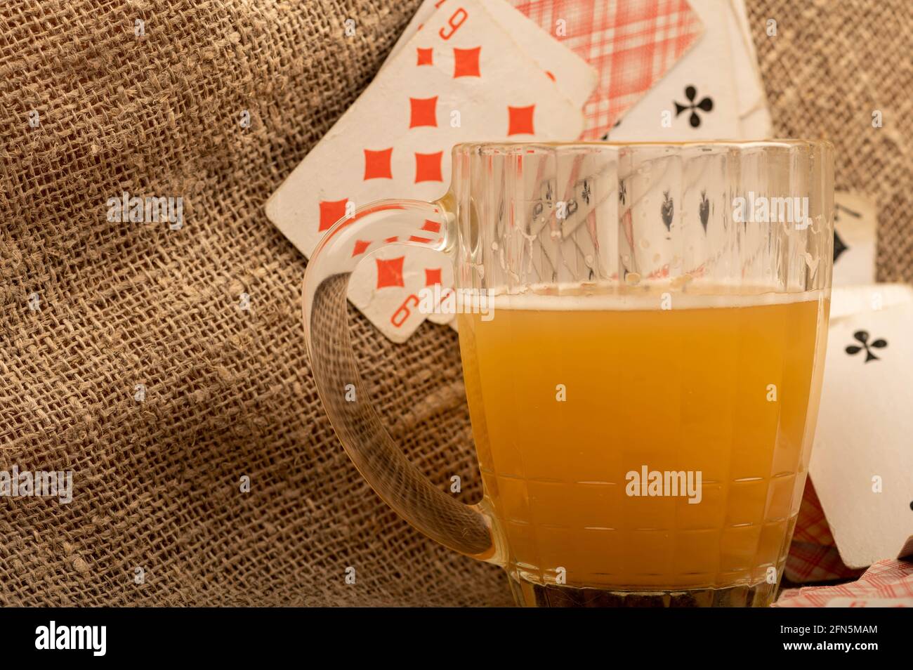 Cartes à jouer et une tasse de bière légère non filtrée sur une table recouverte d'un chiffon épais. Gros plan, mise au point sélective. Banque D'Images