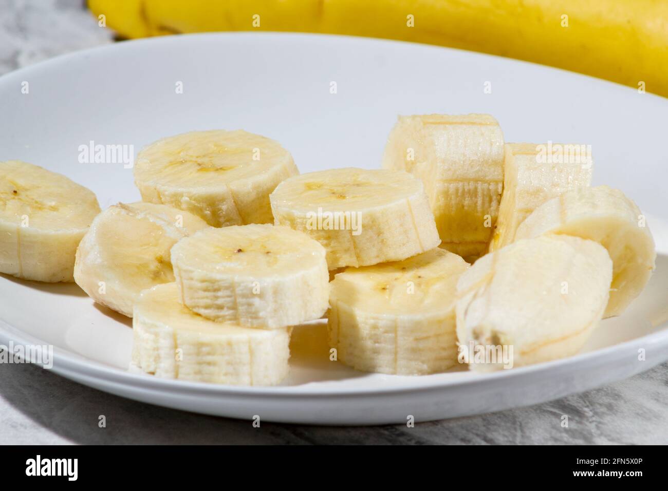 Un bouquet de bananes et une banane en tranches sur une assiette sur une table. Banque D'Images