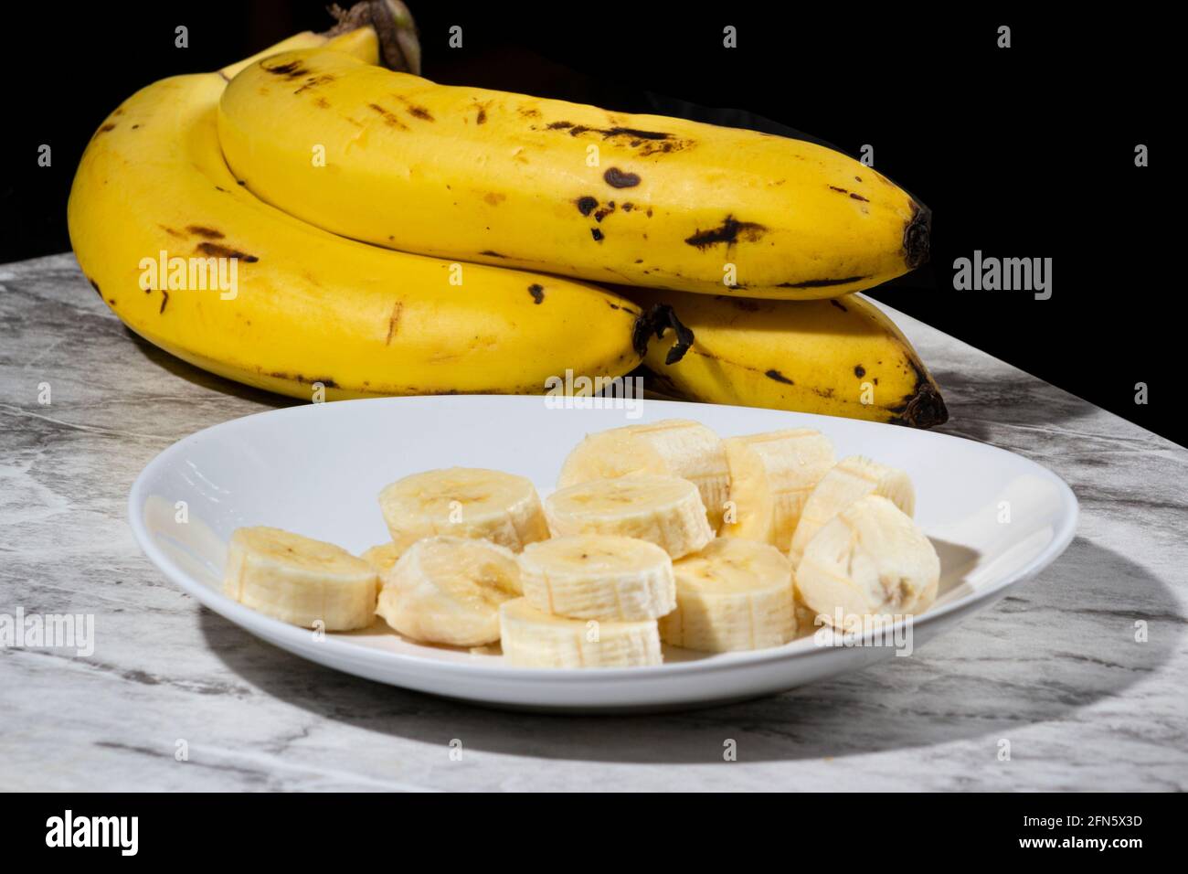 Un bouquet de bananes et une banane en tranches sur une assiette sur une table. Mise au point sélective. Banque D'Images