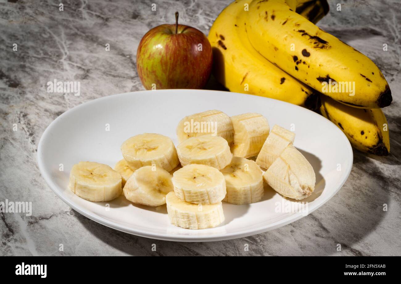 Un bouquet de bananes, une banane en tranches et une pomme sur une assiette sur une table. Mise au point sélective. Banque D'Images