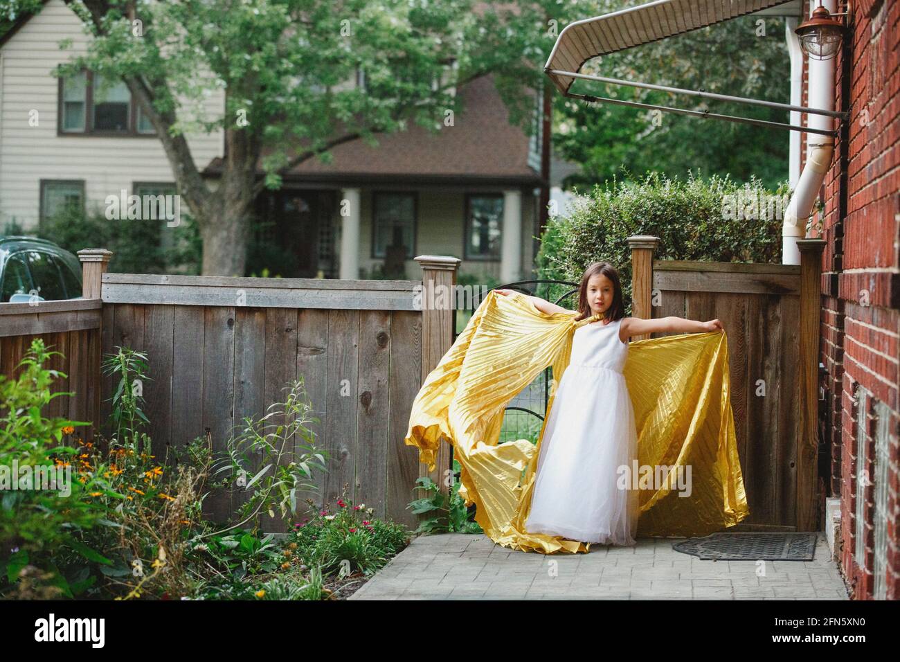 Une petite fille se tient dans les bras de jardin étirés en long cape d'or Banque D'Images