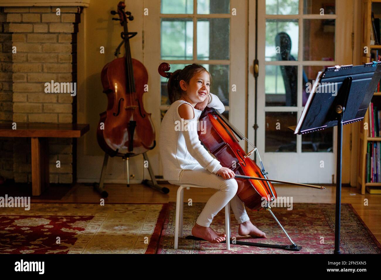 Une heureuse fille pieds nus pratique son violoncelle dans la vie chambre Banque D'Images