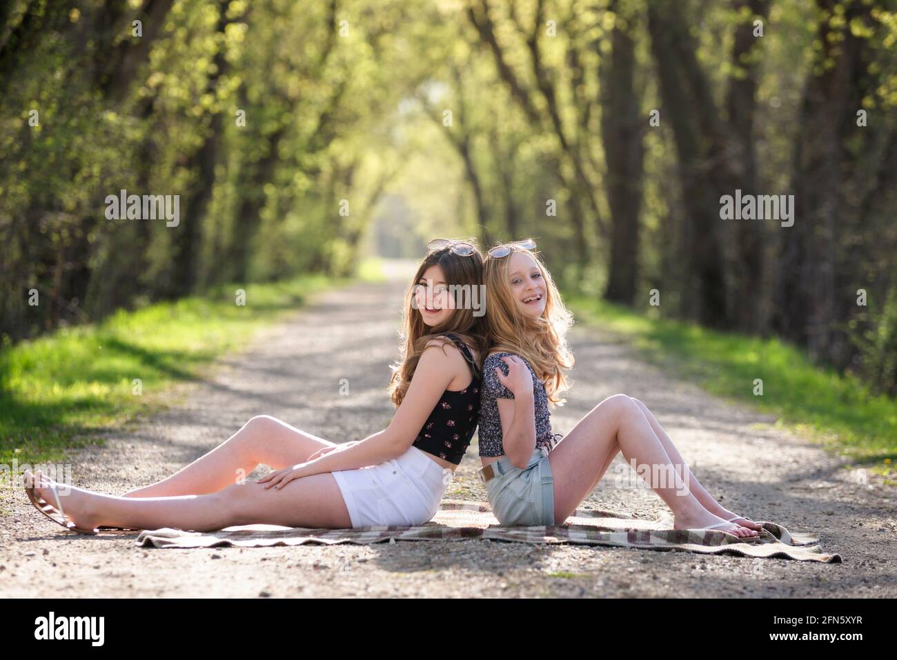 Deux jolies filles adolescentes assises sur une route de campagne bordée d'arbres. Banque D'Images